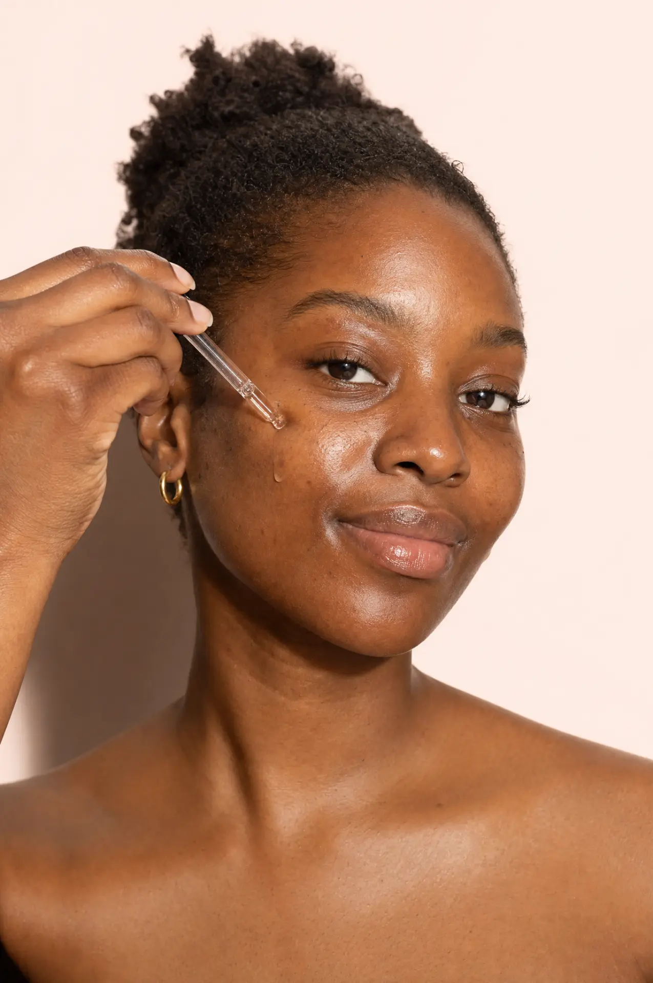 A woman applying a serum droplet to her cheek with a glass pipette